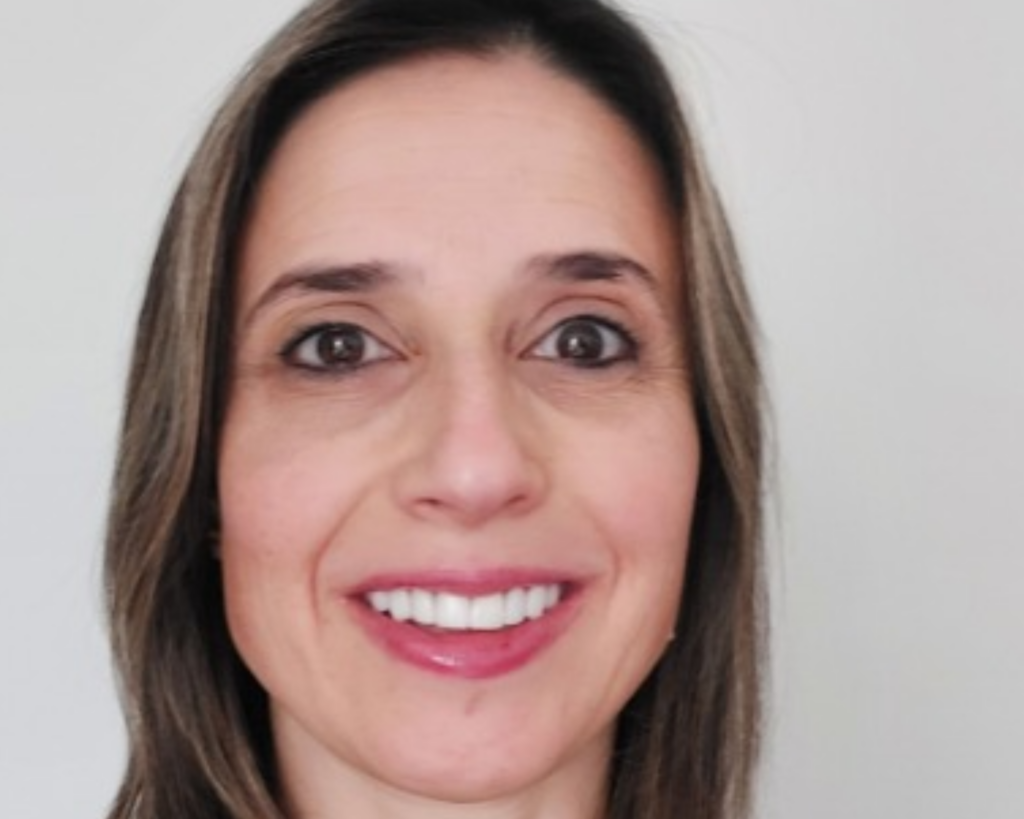 Mulher branca com cabelos pretos, mechas loiras e lisos. Está sorridente.