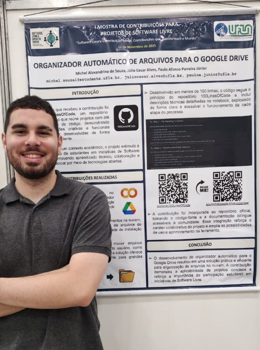 Fotografia de um jovem sorridente, de barba curta e camiseta cinza, posando ao lado de um pôster acadêmico vertical. O pôster, da Universidade Federal de Lavras (UFLA), tem como título "Organizador Automático de Arquivos para o Google Drive". O conteúdo do banner detalha uma contribuição para o repositório "100LinesOfCode", incluindo seções de introdução, contribuições realizadas com logotipos do Google Colab e Drive, códigos QR para acesso ao código-fonte e conclusão. O evento é a "I Mostra de Contribuições para Projetos de Software Livre", realizada em novembro de 2025.